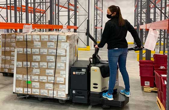 McKesson warehouse employee operating a small forklift, carrying vaccine boxes.