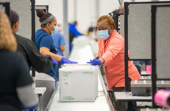 Employees pass Moderna vaccine boxes down the conveyor belt