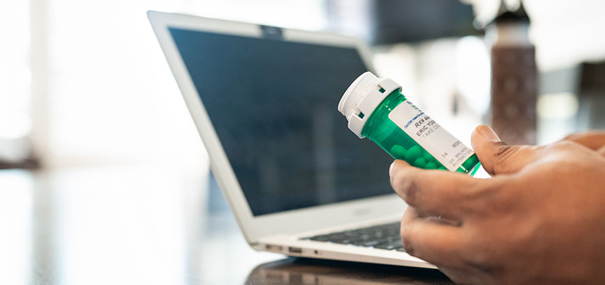 A person holding a prescription pill bottle in front of an open laptop