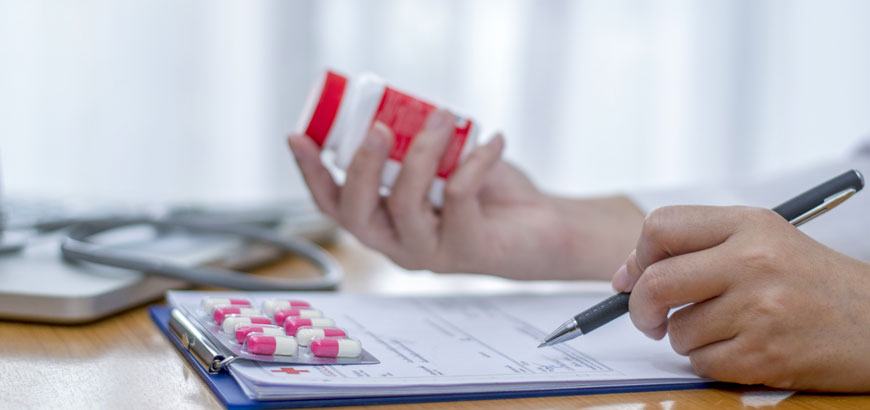 Close up on two hands, one is holding a prescription bottle and the other is filling out a form with a pen.