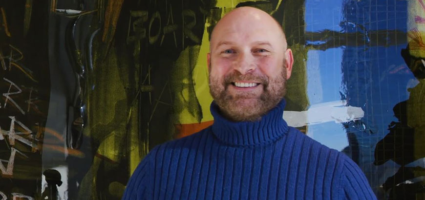 A man wearing a blue turtleneck smiles at the camera.