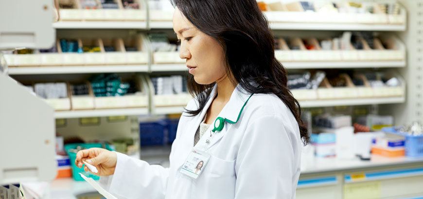 Female pharmacist looks over prescriptions behind the counter.
