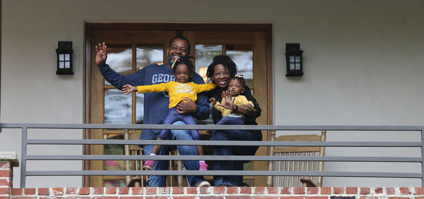 A family standing on a balcony smiling and waving at the camera