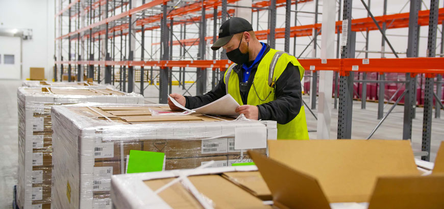 A worker reviewing paperwork while standing in front of a large pallet of boxes