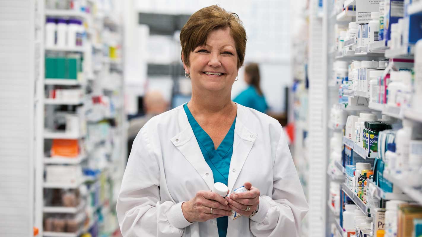 A pharmacist smiling in a pharmacy aisle