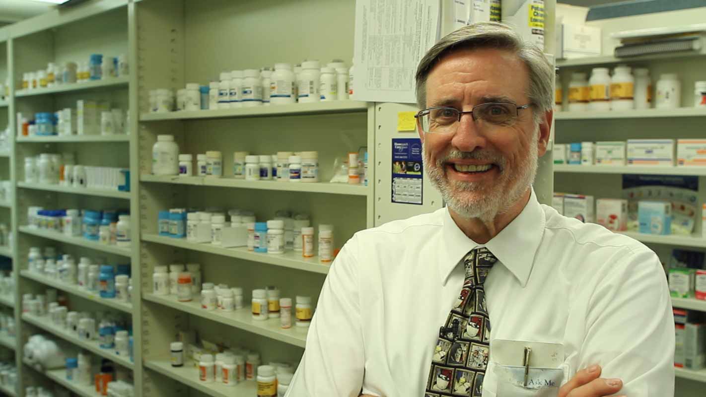 A pharmacist standing in a pharmacy smiling at the camera