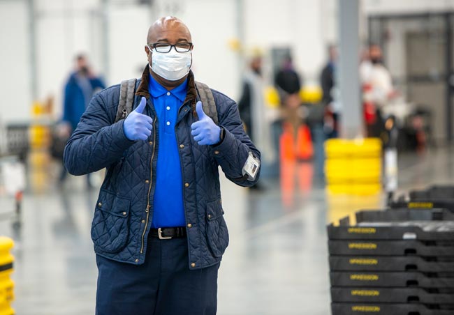 McKesson employee wearing a face mask, winter coat and gloves gives two thumbs up to the camera