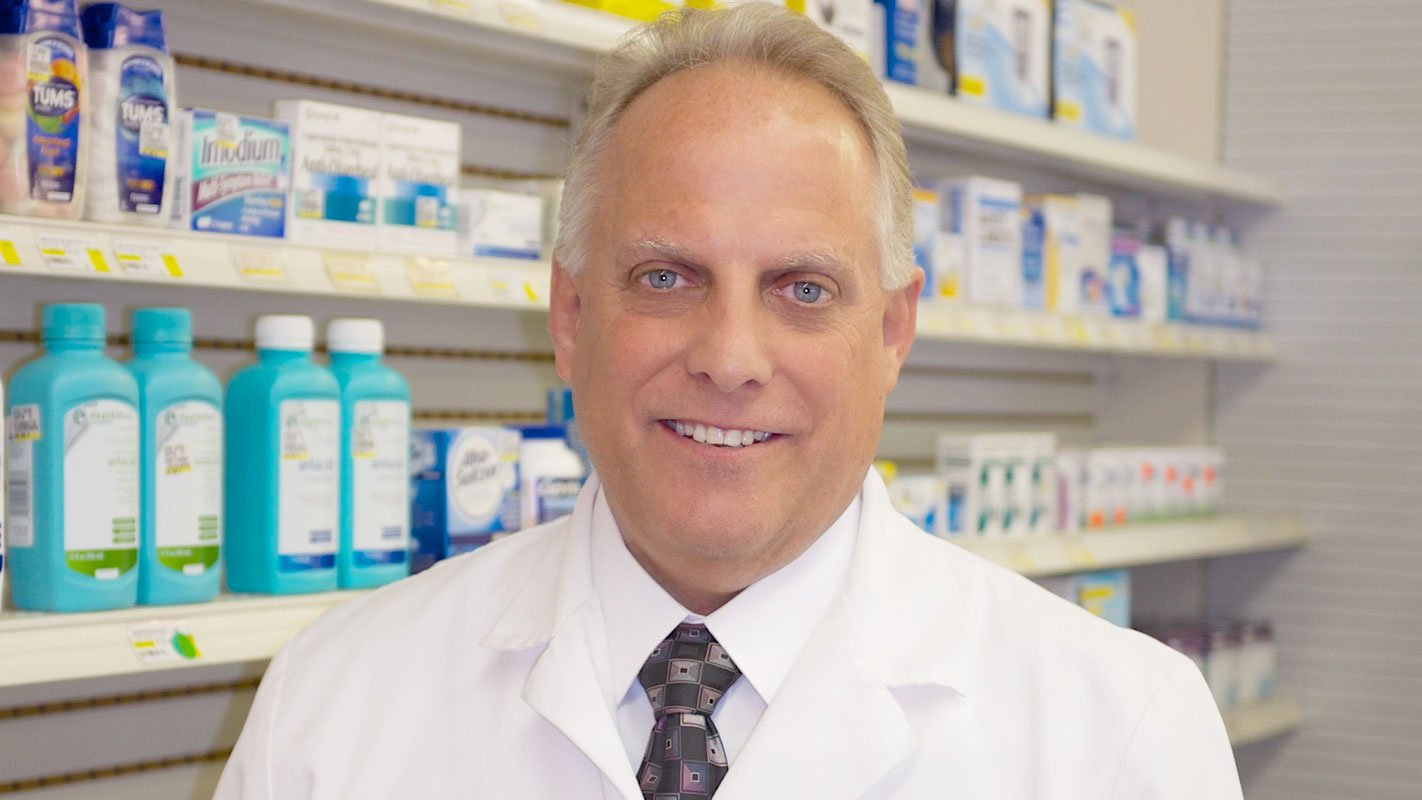 A pharmacist standing in front of a shelf of medications in a pharmacy